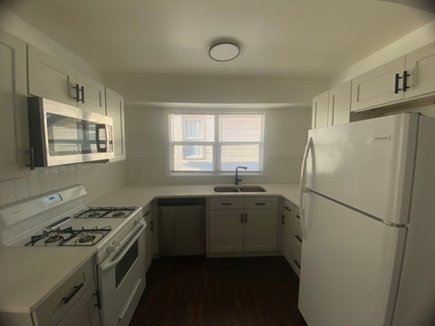 A white kitchen with a stove, sink, and refrigerator.