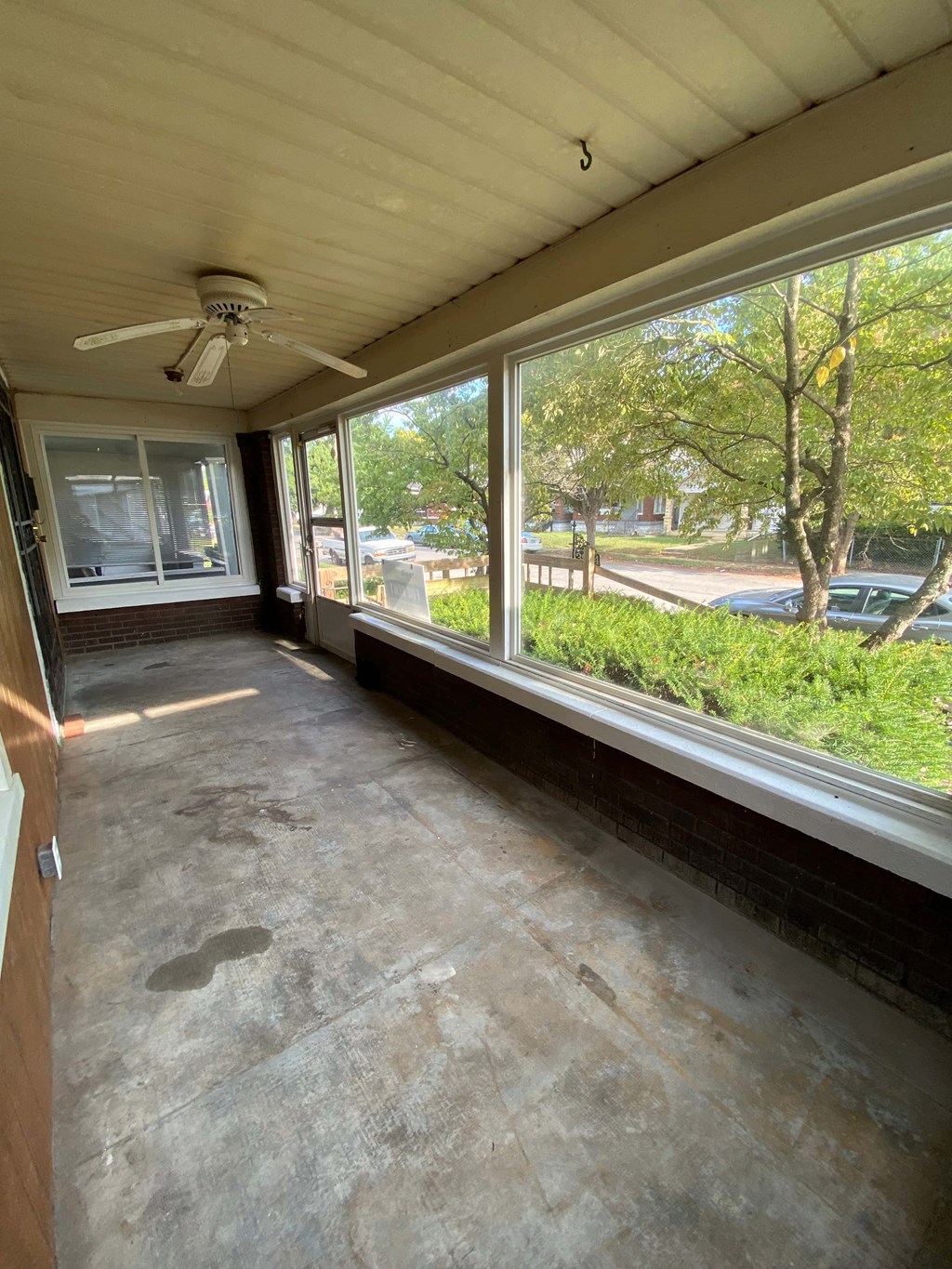 A sunny day in a room with a ceiling fan and a view of the street outside.