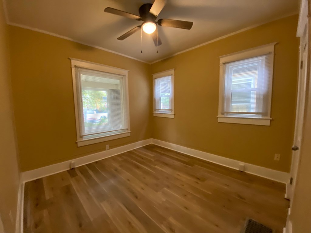 A room with a ceiling fan and two windows.