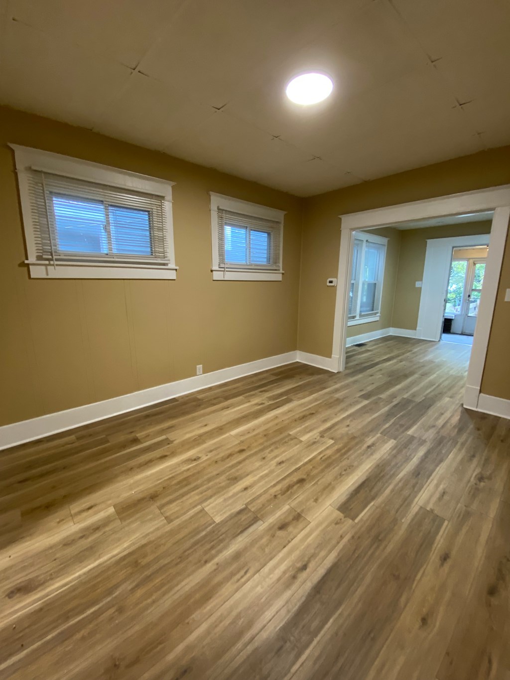 A room with wooden flooring and two windows.