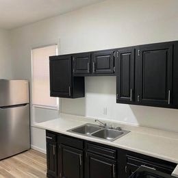 A kitchen with black cabinets and a stainless steel refrigerator.