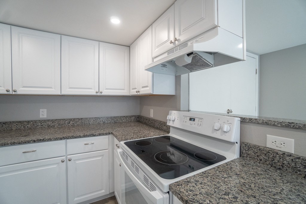 a kitchen with white cabinets and granite counter tops and a white stove and oven