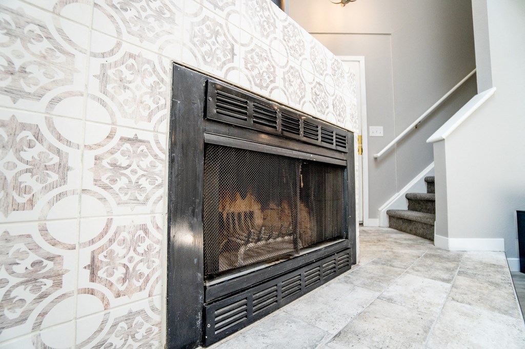 a fireplace in a living room with a tile wall and a staircase