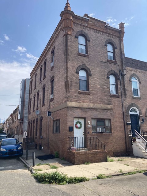 A blue car is parked on the sidewalk in front of a brick building.