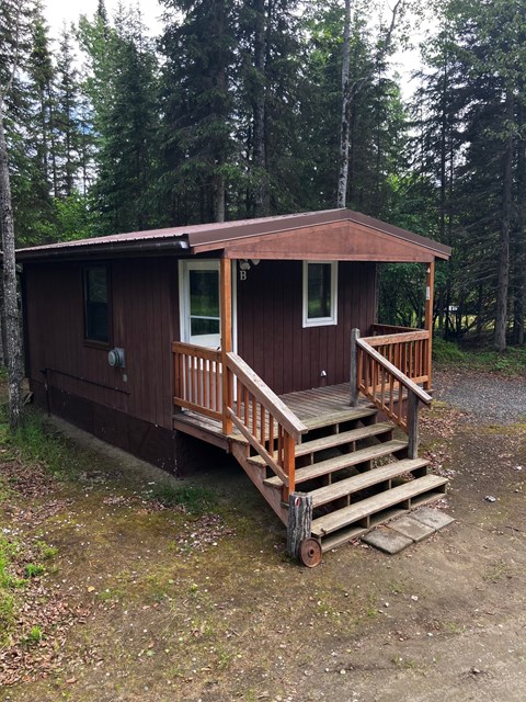 A small brown cabin with a porch and stairs leading up to it.
