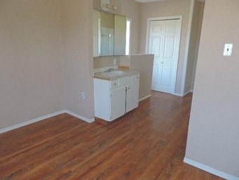 an empty living room with a kitchen with wooden floors