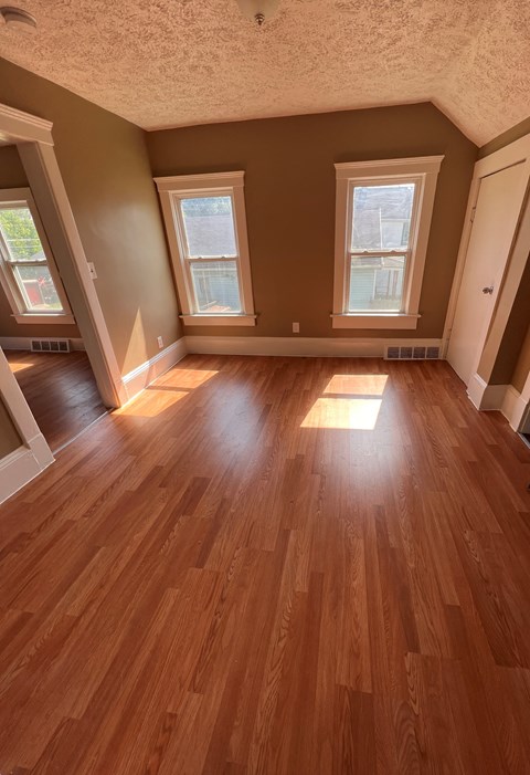 an empty living room with wooden floors and three windows