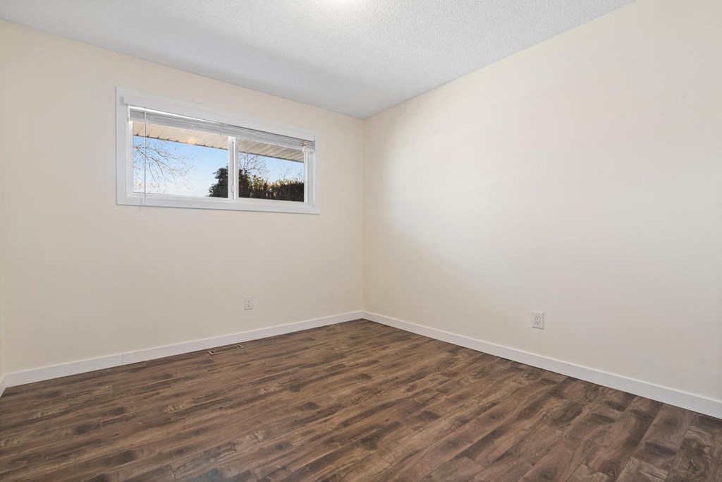 a bedroom with white walls and wood flooring and a window