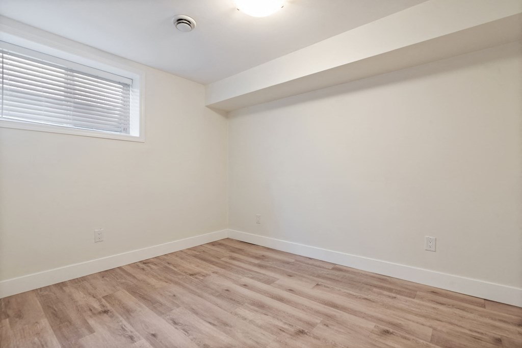 a bedroom with white walls and wood flooring and a window