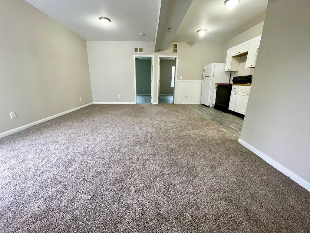 A spacious room with a kitchenette in the background.