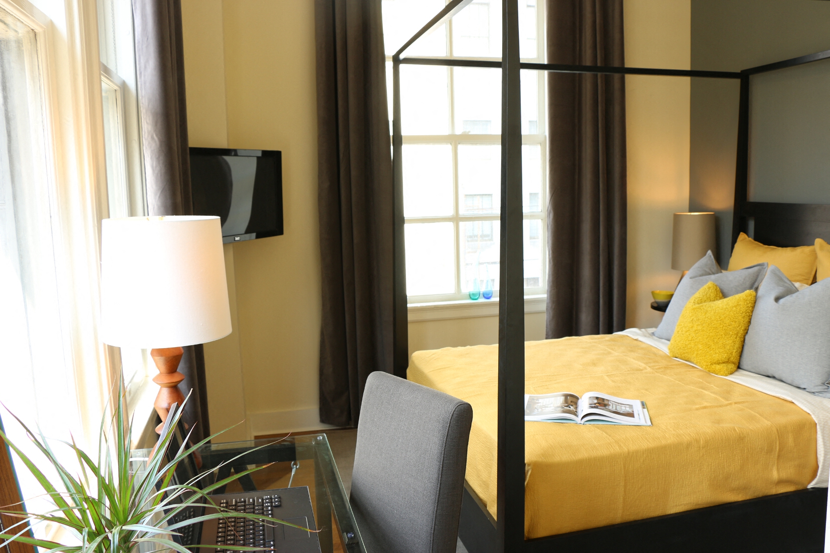 a hotel room with a yellow bed and a glass desk