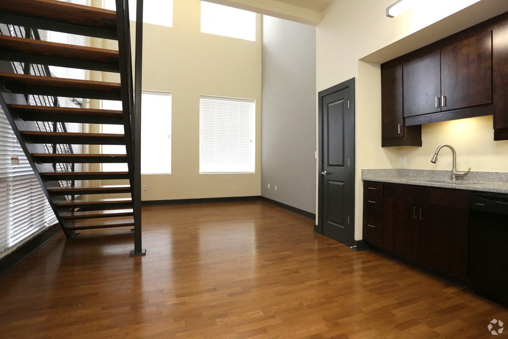 a living room with a staircase and a kitchen with wood floors