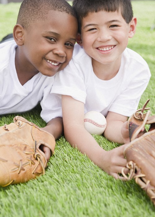 two young boys laying on the grass with a baseball and glove
