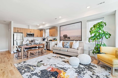 A living room with a rug, a yellow chair, a couch, a dining table and a painting on the wall.