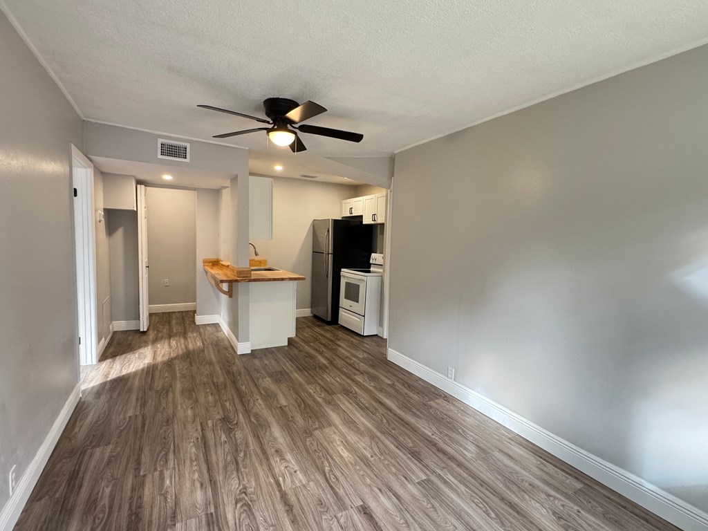 A room with a ceiling fan and a kitchenette.