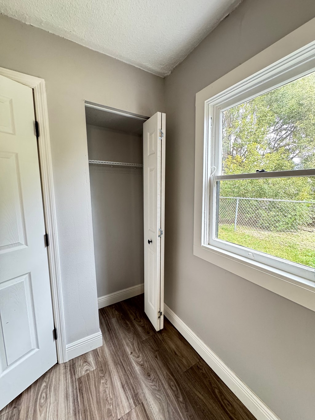 A room with a white door, a window, and a wooden floor.