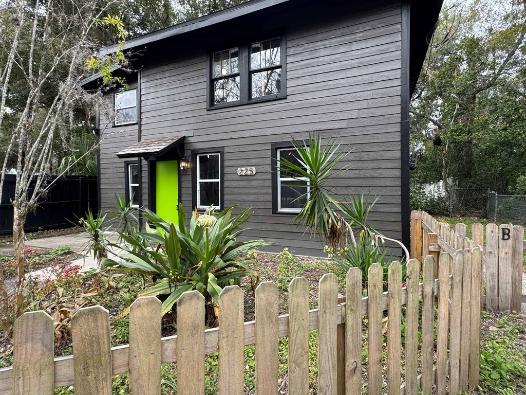 A grey house with a green door and a wooden fence.