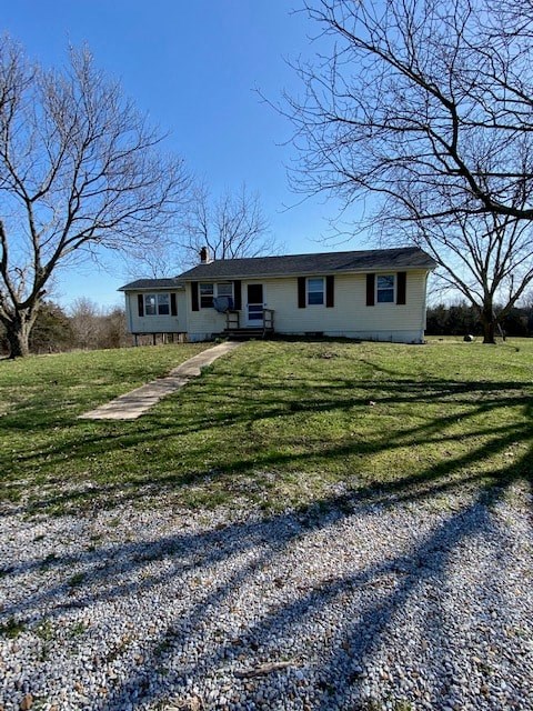 A house with a grey roof and white siding is surrounded by a grassy area and bare trees.