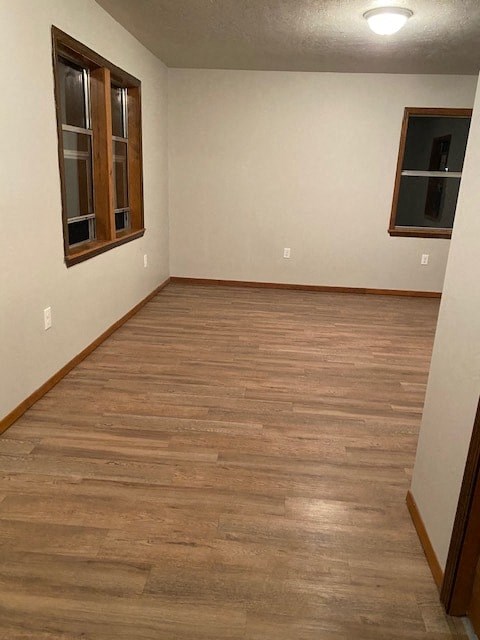 A room with wooden flooring and two windows.