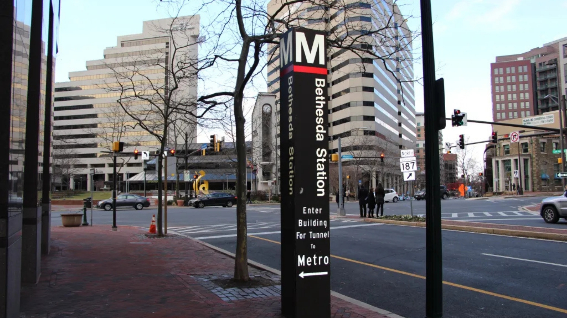 A sign for the Bethesda Station Metro entrance is in the foreground of a city street.