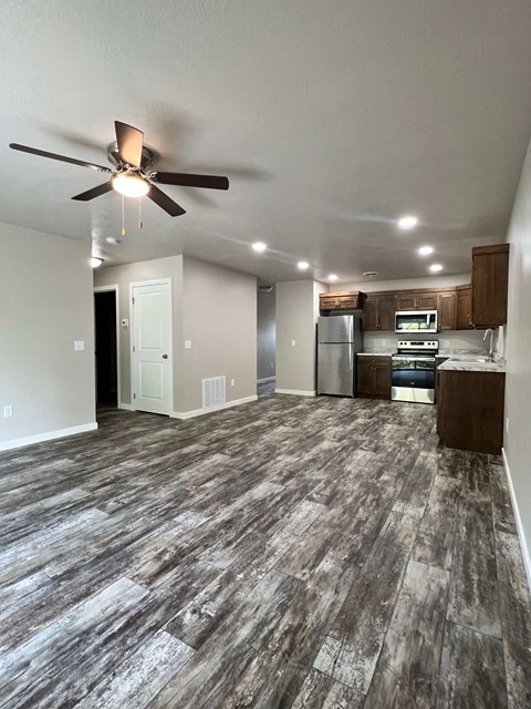an empty living room with a ceiling fan and a kitchen