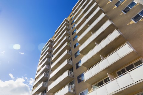 A tall building with balconies and windows under a blue sky.