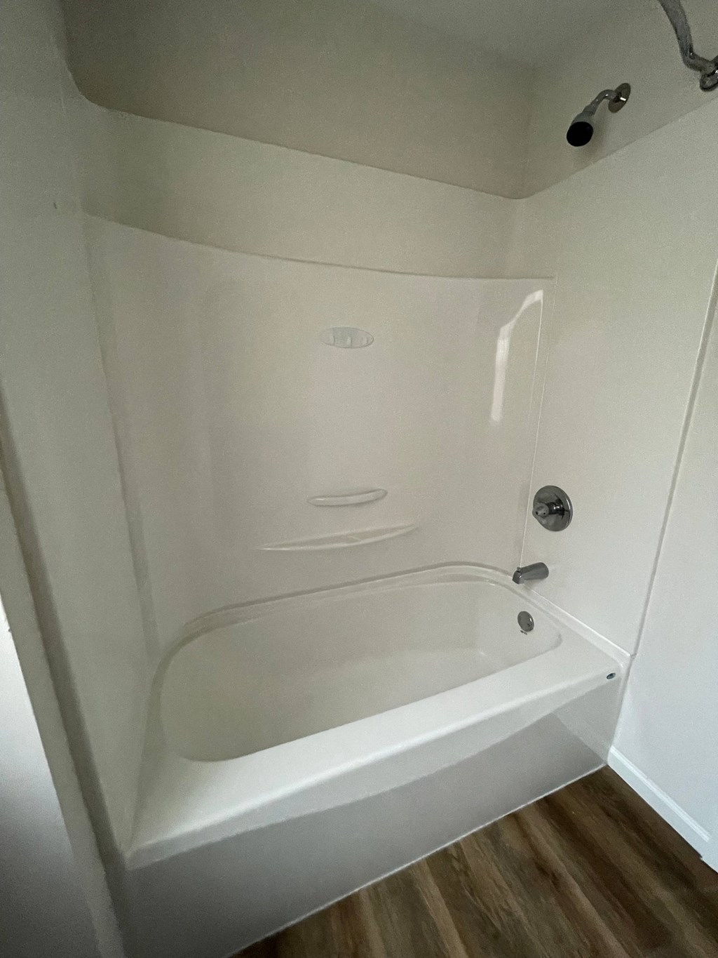 a small white shower in a bathroom with wood flooring
