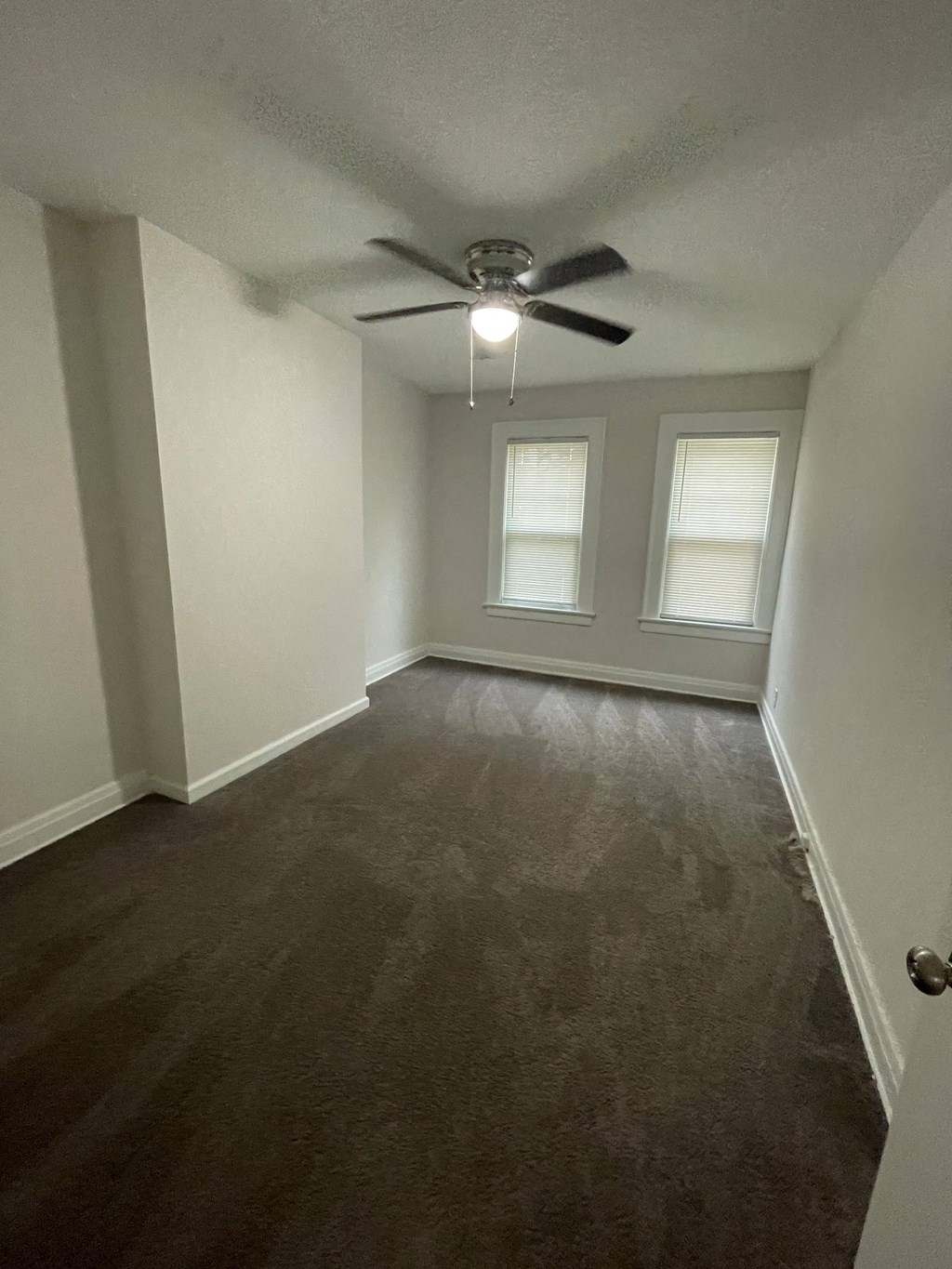 an empty living room with a ceiling fan and two windows