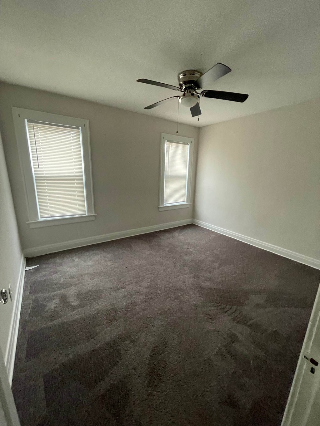 a empty room with a ceiling fan and two windows