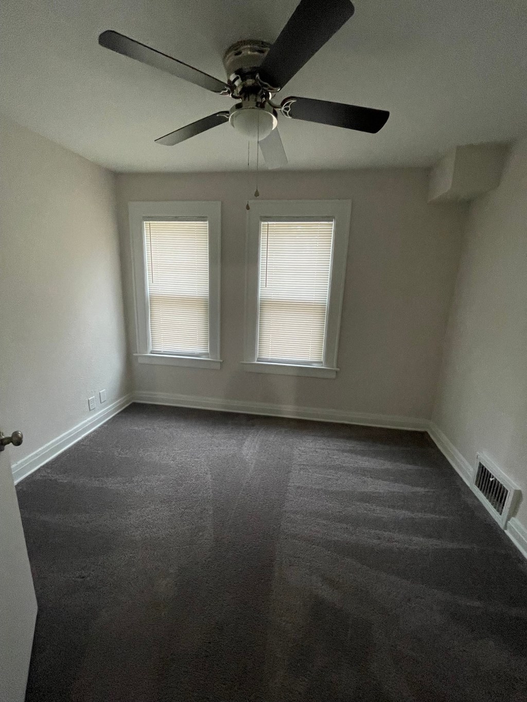 an empty room with a ceiling fan and two windows