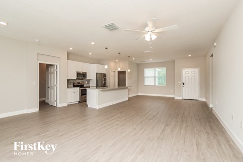 A spacious living room with a kitchen in the background and a ceiling fan above.