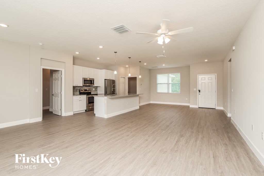 A spacious living room with a kitchen in the background and a ceiling fan above.