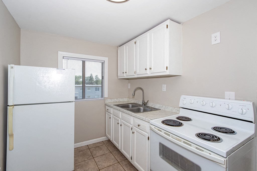 an empty kitchen with white appliances and a refrigerator