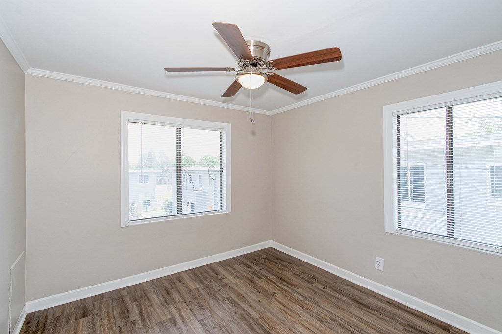 an empty room with a ceiling fan and two windows
