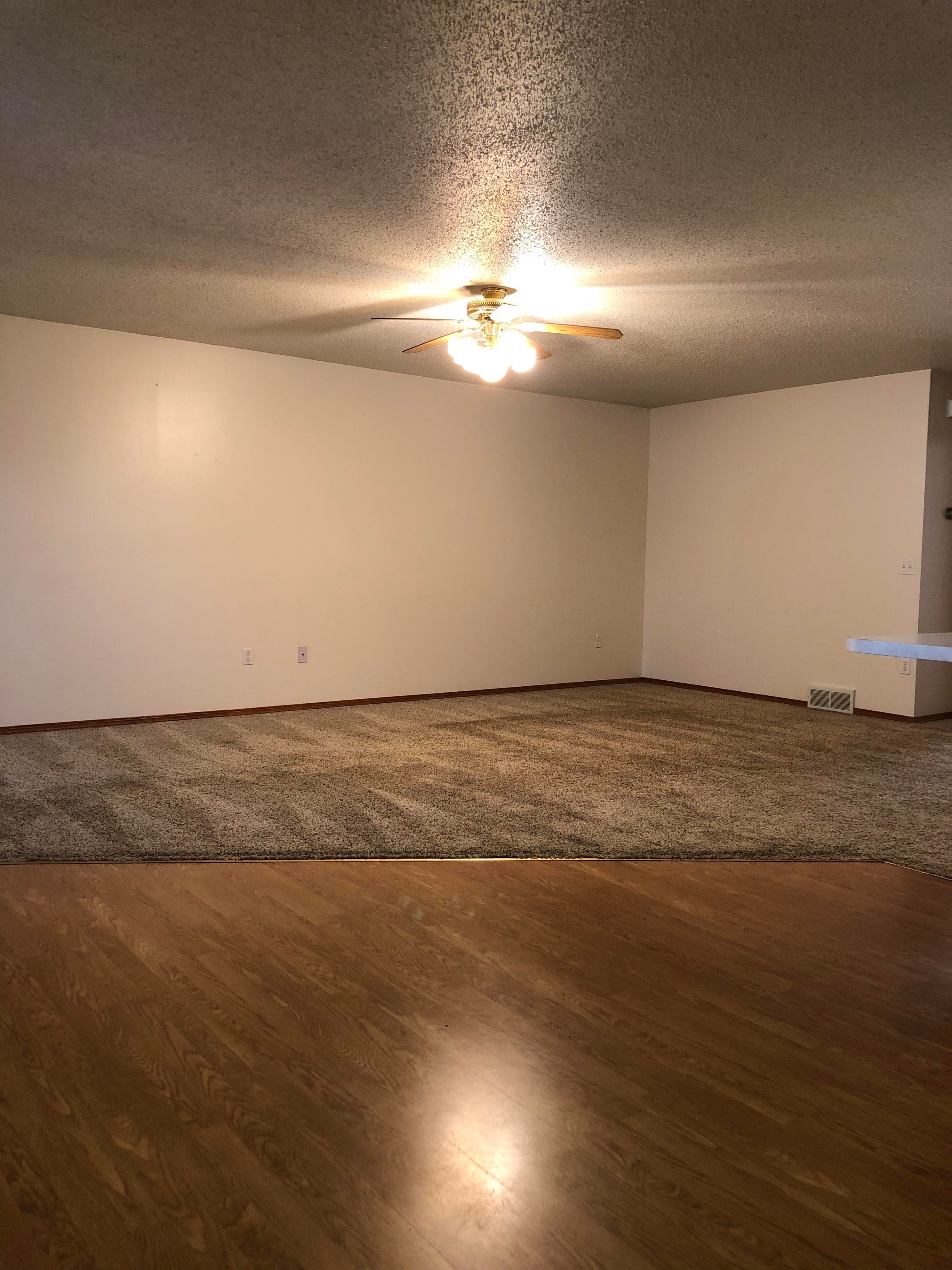 A room with a ceiling fan and a rug on the floor.