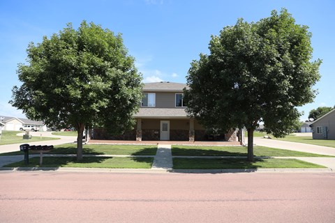 A building is surrounded by two trees and a grassy area.
