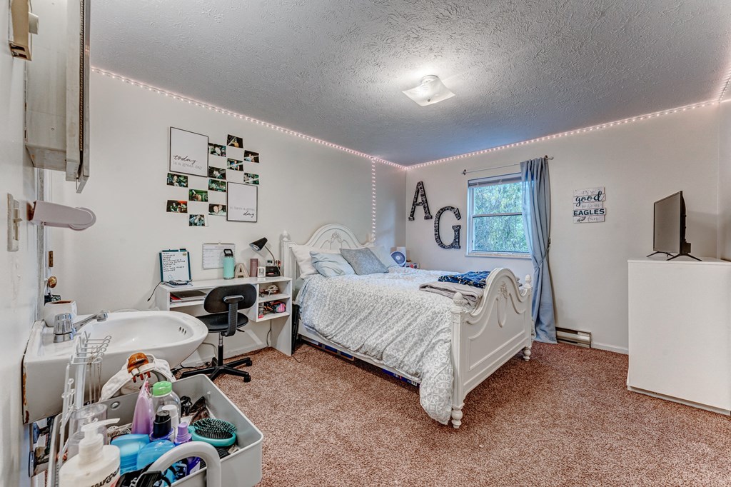 A small bedroom with a bed, a sink, and a TV.