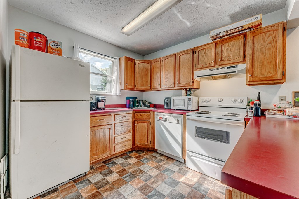 A kitchen with a white refrigerator, wooden cabinets, and a checkered floor.