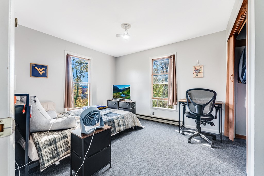 A bedroom with a bed, chair, and two windows.