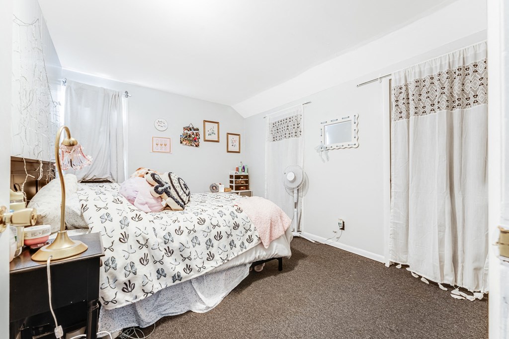 A bedroom with a bed, a desk, and a window with curtains.
