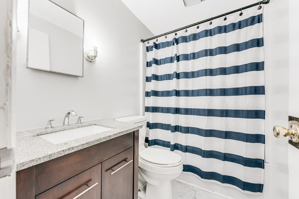 A white toilet sits under a blue and white striped shower curtain in a bathroom.