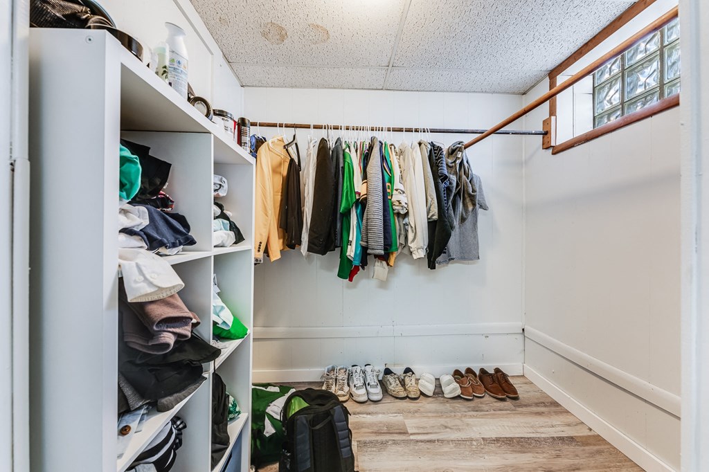 A white closet with clothes and shoes.