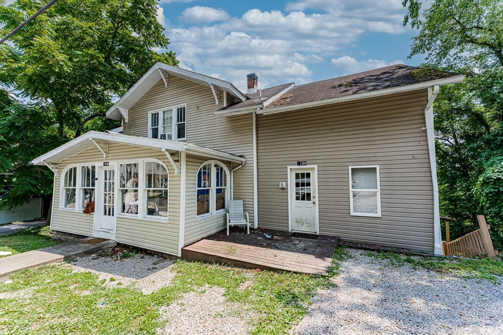 A house with a grey siding and a white door is surrounded by greenery.