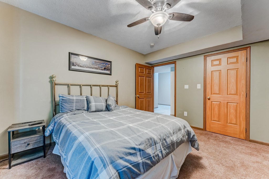 A bedroom with a bed, a ceiling fan, and a painting on the wall.