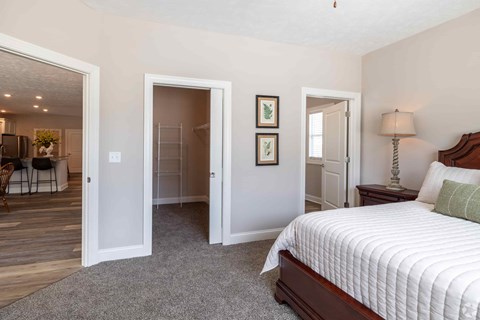 A bedroom with a large bed and a dining area in the background.