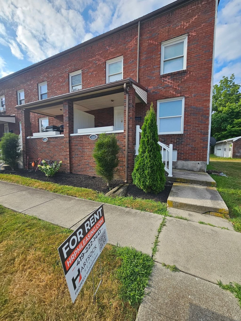A red brick building with a for rent sign in front.