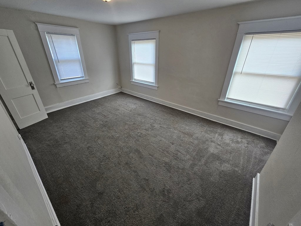 A room with grey carpet and three windows.