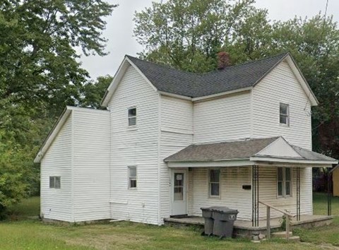 a white house with a porch and a trash can