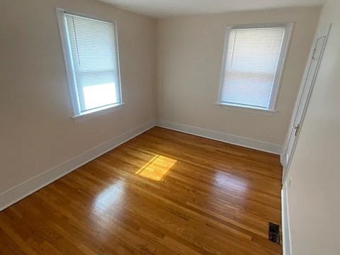A room with wooden flooring and two windows.
