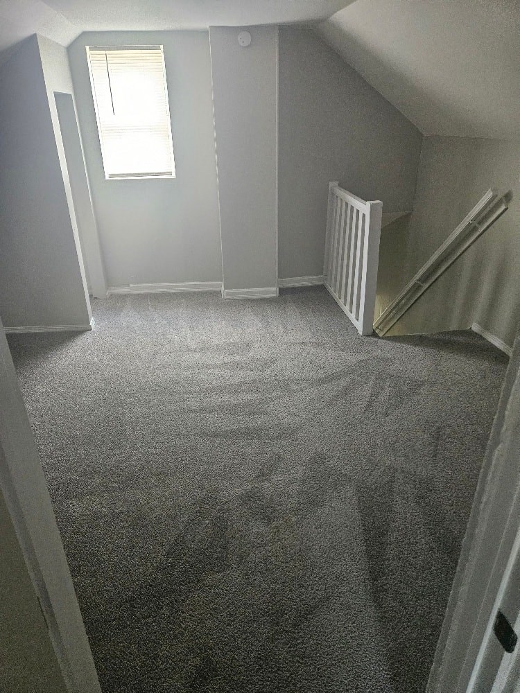a carpeted room with a staircase and a window